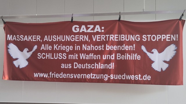 Ein Banner der „Friedensvernetzung Südwest” mit dem Text „GAZA: Massaker, Aushungern, Vertreibung Stoppen! Alle Kriege in Nahost beenden! SCHLUSS mit Waffen und Beihilfe aus Deutschland!”

Darunter die Domain der Webseite: www.friedensvernetzung-suedwest.de
