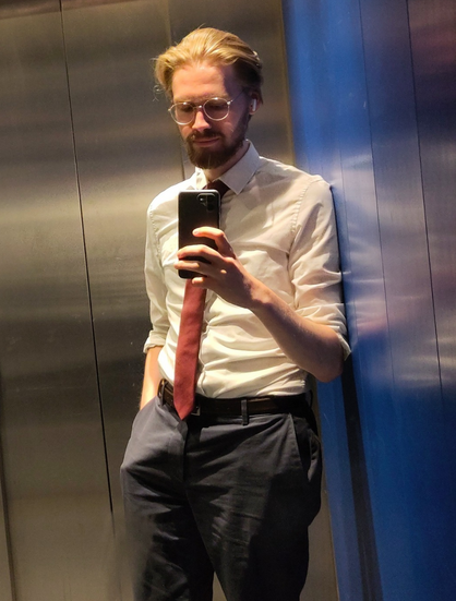 A picture of Erik Uden in an elevator with his hand in his pocket wearing a tie going above his belt.