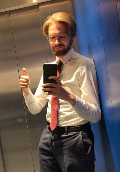 A picture of Erik Uden in an elevator showing a thumbs up wearing a tie going above his belt.
