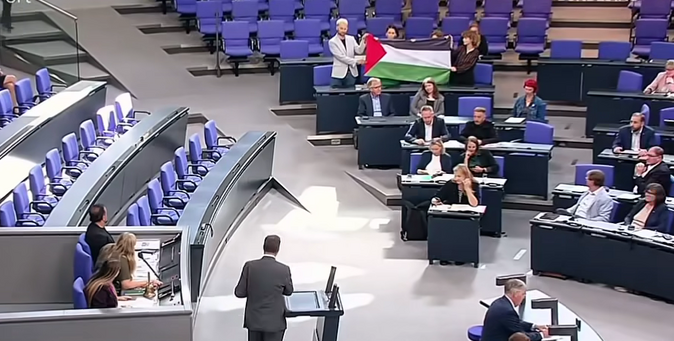 Ein Bild vom Plenarsaal des Bundestags auf dem eine Palästina-Flagge innerhalb der Fraktion von Die Linke gehoben wird.