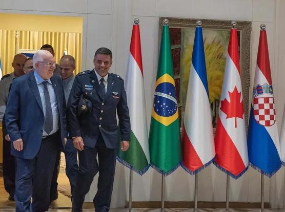 A picture of military generals walking out of a room with several flag cones from Italy, Brazil, France, Canada, and Serbia being displayed