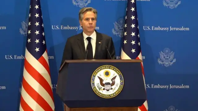 A picture of Anthony Blinken at a press conference of the US Embassy of Jerusalem with almost real looking flags in the background, but since this picture is taken at an angle, one can see that they're cones