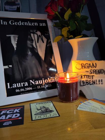 Ein Bild von der kleinen Gedenkstelle für Laura Naujokat, vom 5. November 2025 im Unabhängigen Jugendzentrum Kornstraße (UJZ Korn). Es steht ein weißer Bilderrahmen mit schwarz-weißem Bild von Laura vor einer Wand mit Graffiti mit der Auffschrift „In Gedenken an Laura Naujokat” 06.06.2006 bis 11.10.2025. Im Kleingedruckten steht auch „Bild vom 20.09.2025 während der Hausbesetzung in der Nieschlagstraße”. Es ist das Bild auf dem Laura mit dem Journalisten von der HAZ spricht.

Rechts neben dem B…