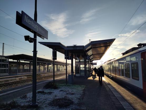 Ein Bild des Bahnsteigs der Stadt Nienburg bei einem Winter Sonnenaufgang mit leicht eingefrorenem Tau auf dem Rasen und der hellsten Sonne am tiefen Horizont