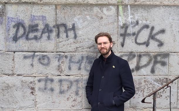 Ein Bild mit Erik Uden wie er vor einer Wand steht auf der „DEATH TO THE IDF” und „FUCK IDF” (Tod der Israeli Defense Force und Fick die Israeli Defense Force) geschrieben ist.
