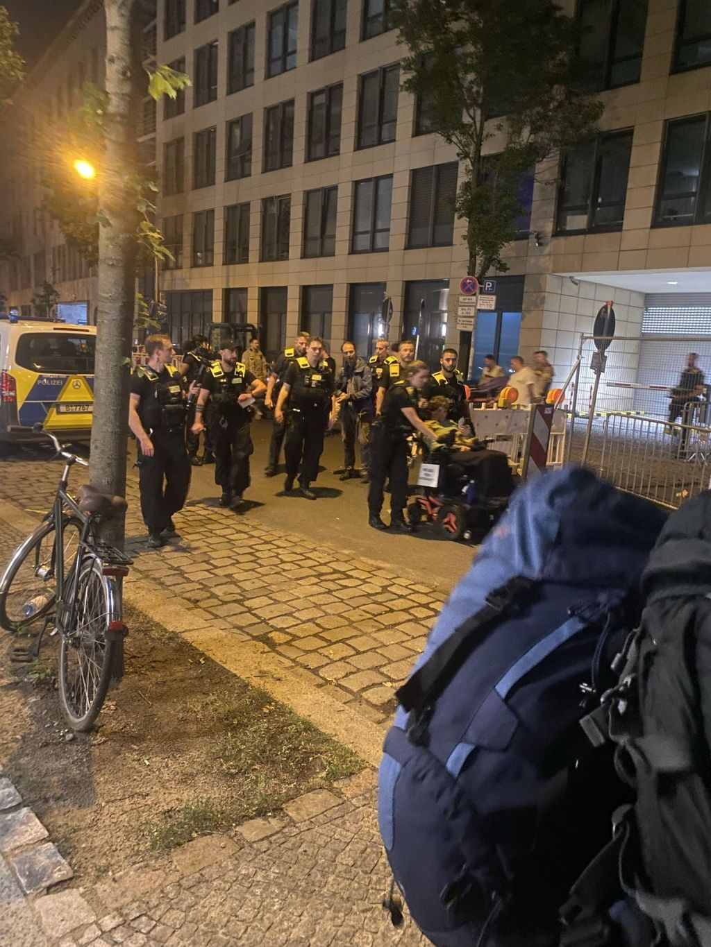 ein Dutzend Polizeist*innen begleiten eine Person im E-Rollstuhl raus