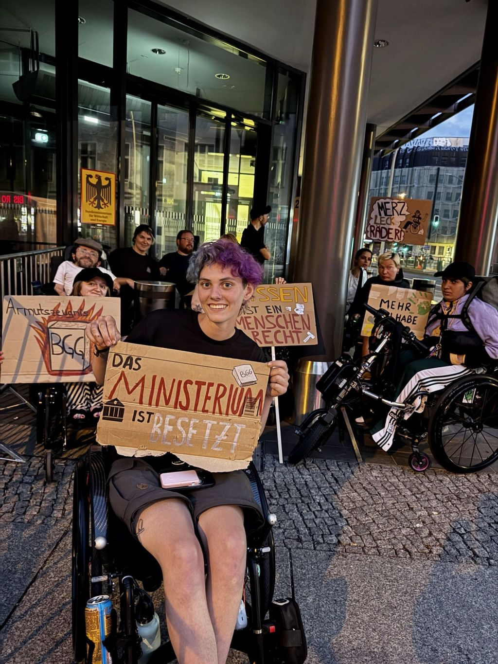 Mahnwache , him hintergrund das Schild vom ministerium. Vorne Menschen mmit Plakat "Das Ministerium ist besetzt"