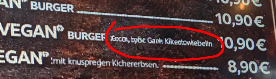 A picture with a red circle surrounding AI messy text that's unreadable. It's saying “Vegan Burger zeccGi, tybc, Gaeh, Kikitowiebeliin” which is no word in no language. This picture was taken in Manhatten Burger in Linden, Hannover.