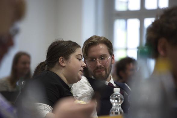 Ein Bild von Johanna Rathkamp und Erik Uden wie sie miteinander sprechen, währenddessen alle anderen Unscharf sind und nur sie im Fokus.